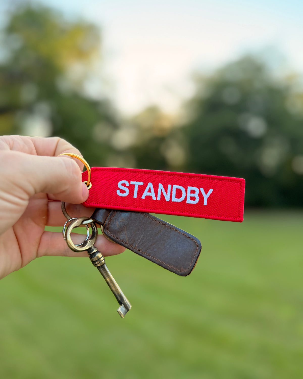 Roter „Standby“ Schlüsselanhänger mit weißer Stickerei und goldfarbenem Ring am Schlüsselbund